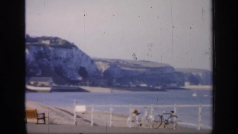 1949 England coastal view with bay water, chalk cliffs, promenade railings, benches, and bicycles in soft 8mm color.
