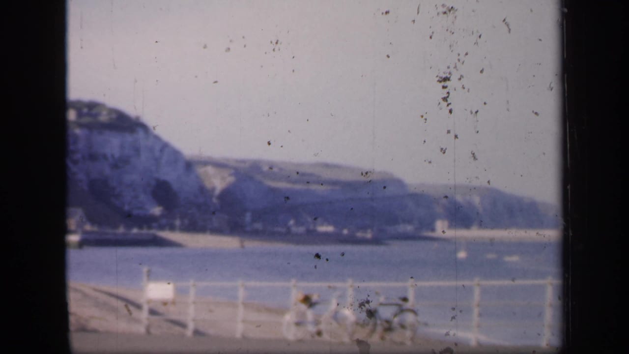 Seafront railing with bicycles, calm water, and distant chalk cliffs.
