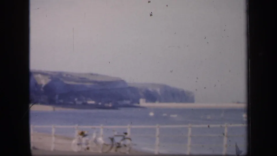 A 1949 English coastal view shows two bicycles near promenade railings, with blue water and chalk cliffs in the distance.