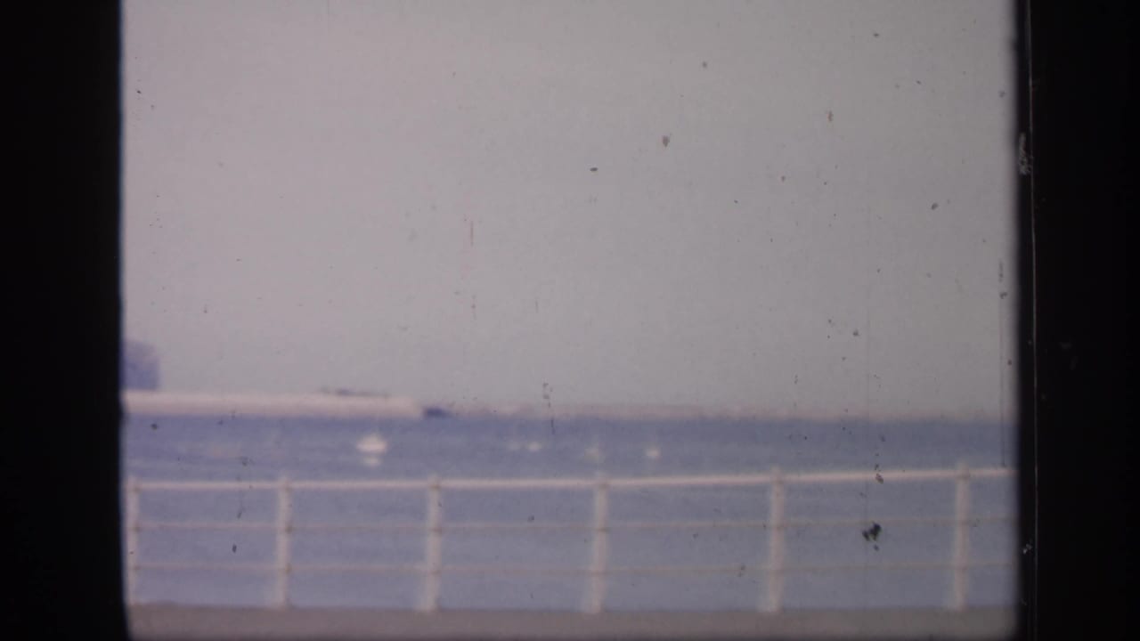 White pier railing overlooking calm water with a faint horizon and dark film borders.