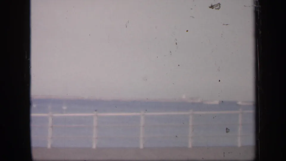1949 England coastal view with a white railing in the foreground, blue water beyond it, and a low distant shoreline or horizon.