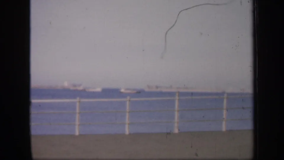 1949 England 8mm still with several distant boats across the water, a white pier railing, pale sky, and visible film scratches.