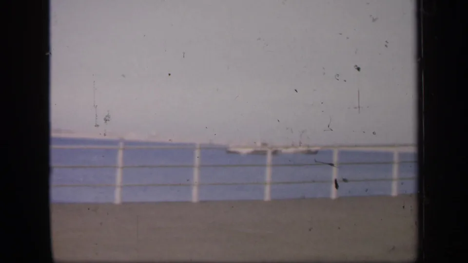 1949 England 8mm frame with a pale sky, water, railing and small boats, partly obscured by the film gate.