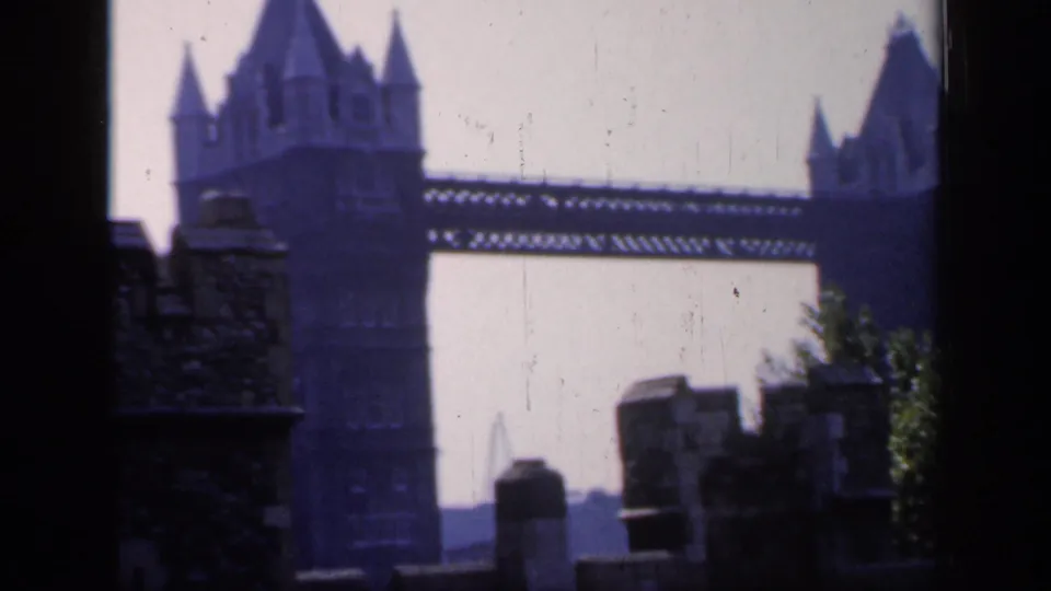 1949 8mm frame of Tower Bridge beyond foreground stonework and greenery, filmed from a visitor's constrained viewpoint.