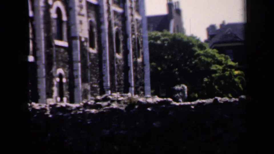 1949 England travel-film frame showing an unidentified historic stone building with arched windows and greenery.