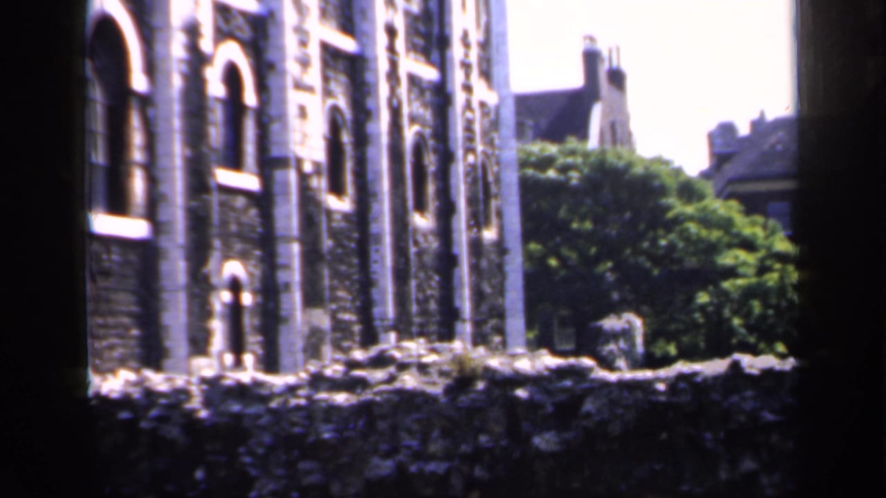 Stone building with arched windows behind a low wall and trees.