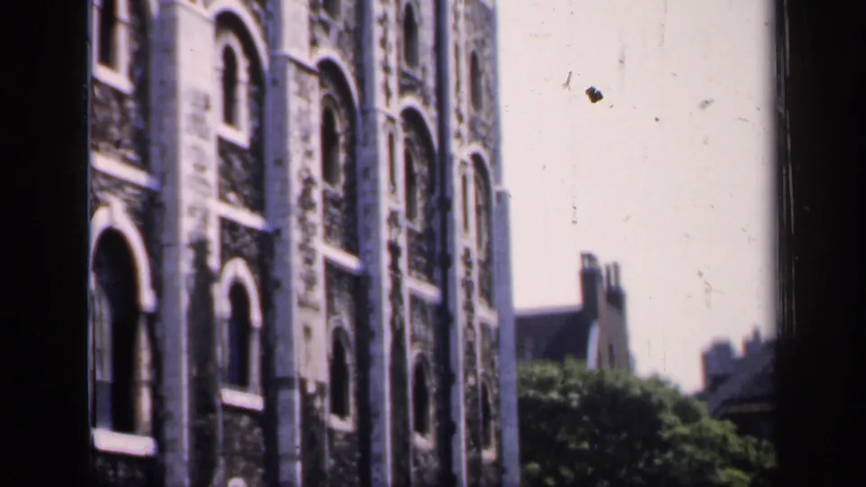 1949 England 8mm view of a stone building edge with repeated arched windows, trees below, and rooftops in the background.