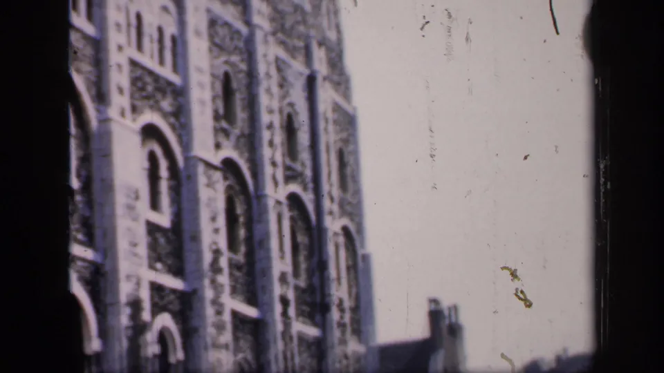 1949 England frame with soft-focus arched stone windows, bright sky, rooftop silhouettes, and visible film dust.