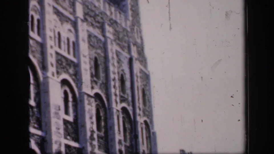 1949 England home-movie frame showing a large historic stone building with arched windows, textured masonry, and a tower.