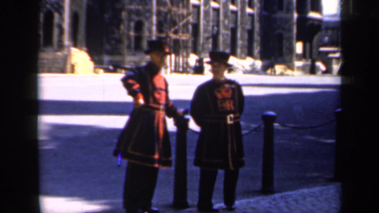Two Yeomen Warders stand near chained bollards outside stone fortress walls.