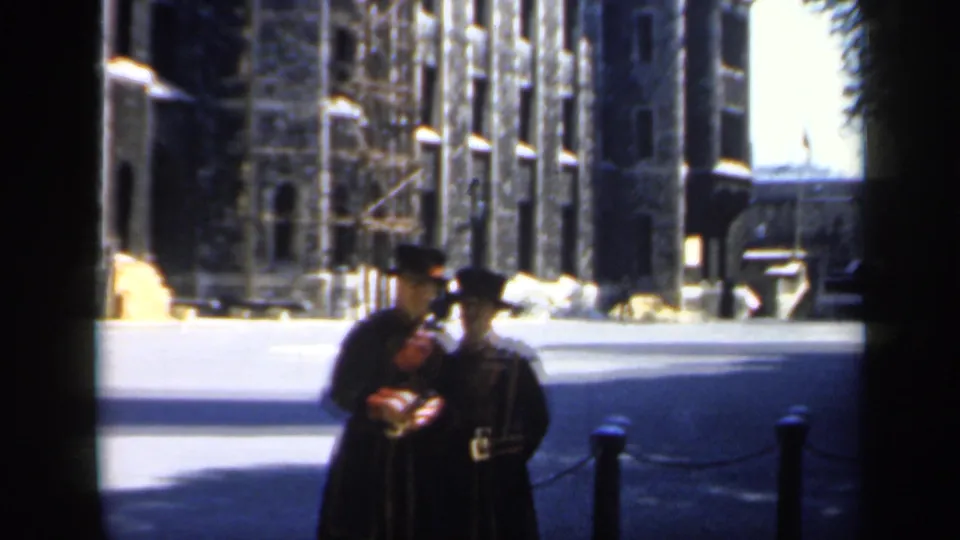 A 1949 England home-movie frame shows one Yeomen Warder leaning toward another in a stone courtyard setting.
