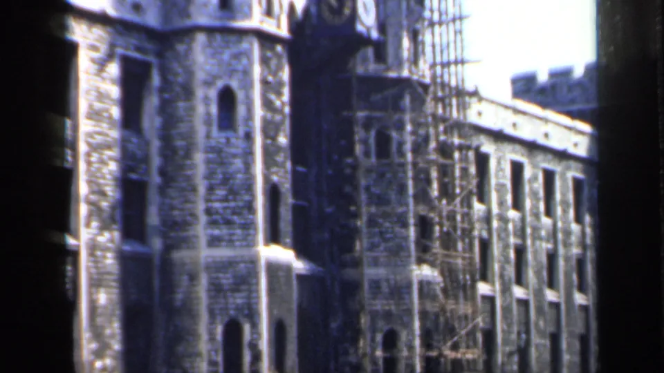 1949 England 8mm frame with a castle-like stone tower, arched windows, scaffolding, and a long adjoining facade.