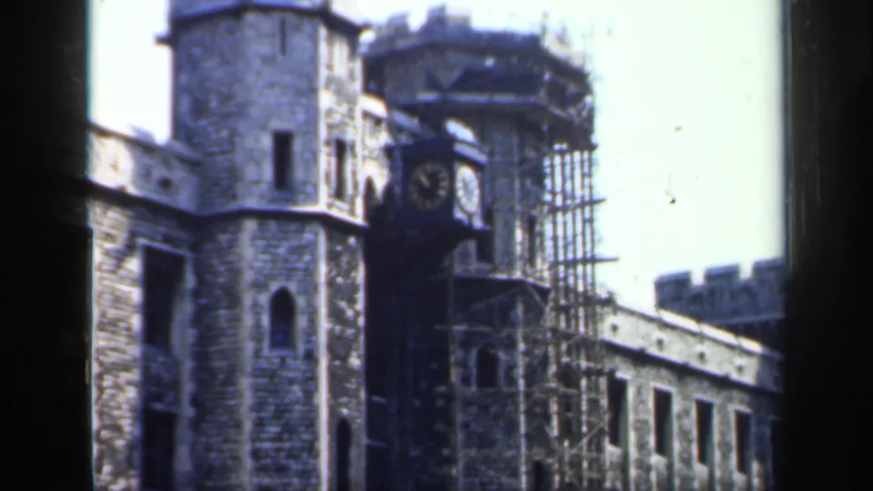 1949 England 8mm frame showing a historic stone tower, projecting clock face, scaffolding, and partial building wing.