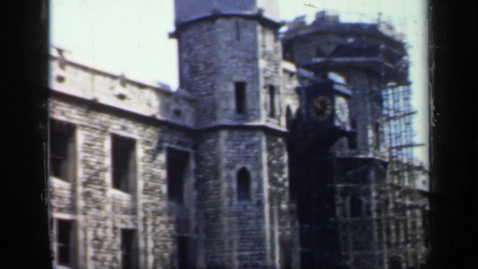 1949 England 8mm frame of a historic stone building with a clock projection, scaffolding, arched windows, and crenellated roofline.