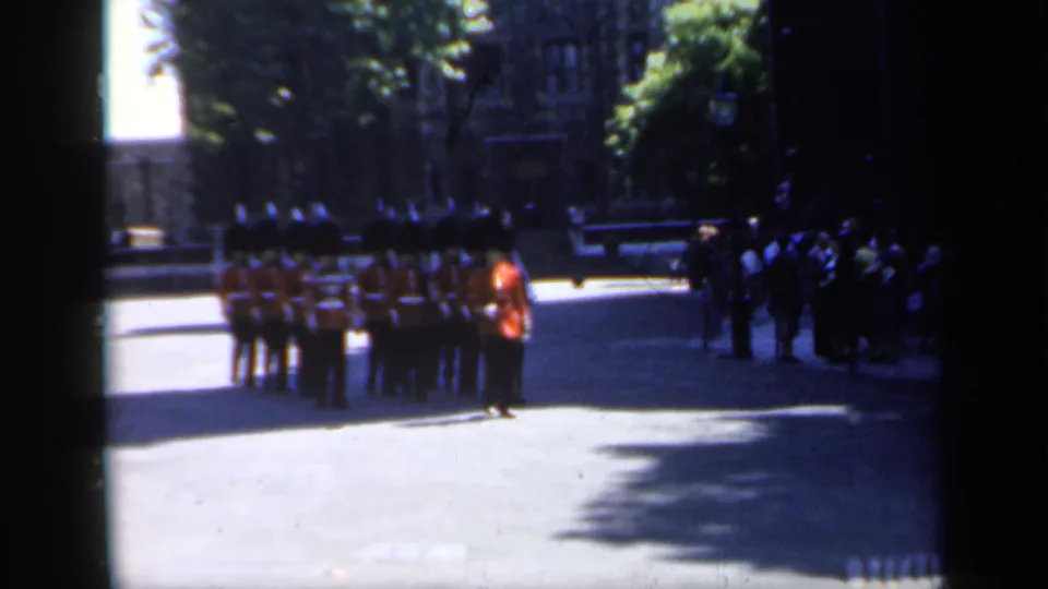 A compact formation of British ceremonial soldiers in red coats is seen near spectators at a historic English site.