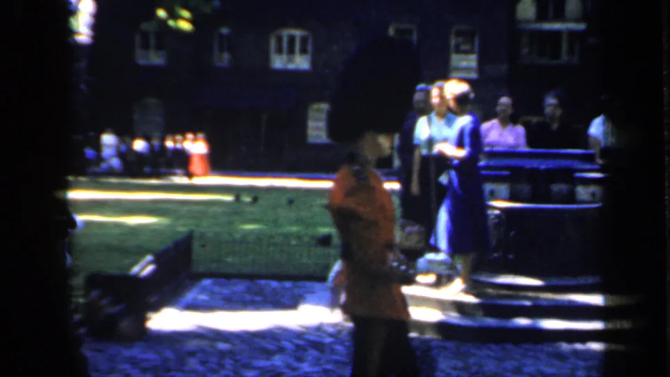 1949 England frame showing visitors beside steps and a lawn, with British guards in red tunics small in the background.
