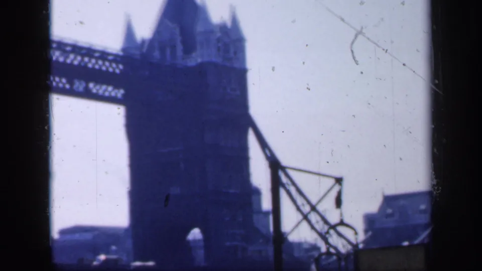 1949 London 8mm frame with a closer view of Tower Bridge tower, upper walkway, bridge structure, and nearby riverside elements.
