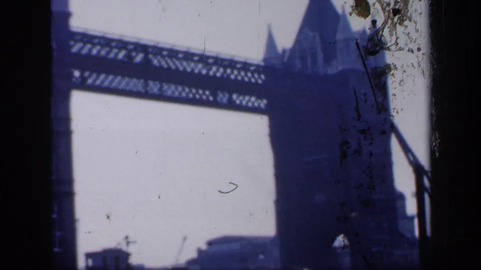 Blue-tinted 1949 London frame showing Tower Bridge's upper span and a tower silhouette, with film dirt and dark edges visible.