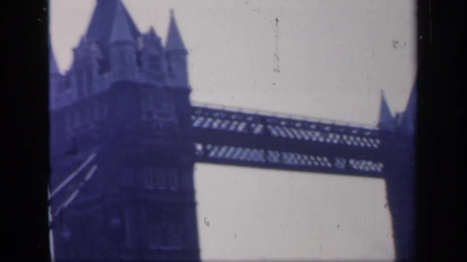 1949 England home-movie frame with a closer view of a Tower Bridge tower, upper walkway, diagonal structure, and worn film surface.