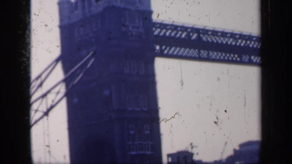 Blue-tinted 1949 London frame showing Tower Bridge tower details, upper walkway, diagonal supports, pale sky, and visible film wear.
