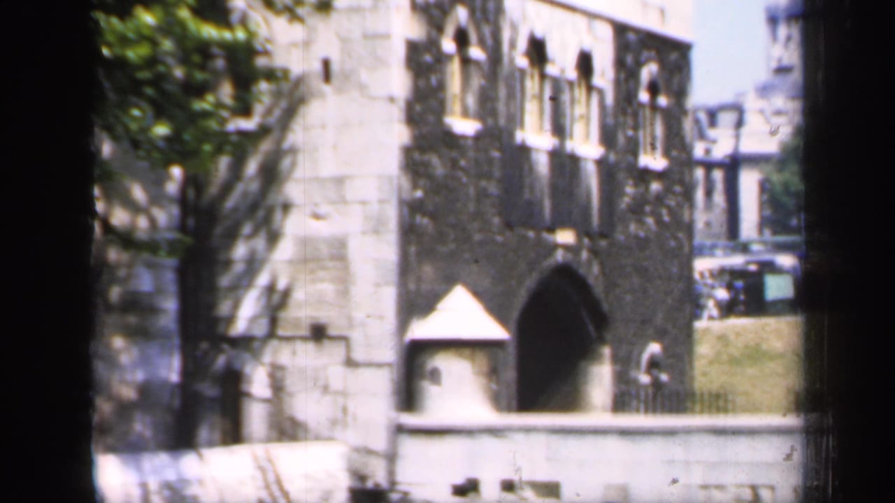 Color 8mm view of a historic English stone facade with arched doorway, small turret-like feature, and sunlit trees.