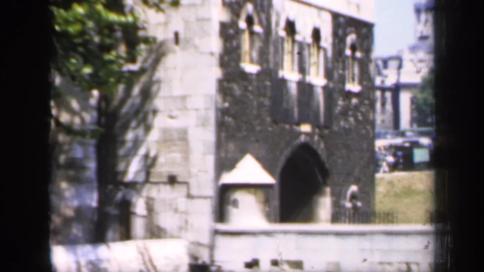 Color 8mm view of a historic English stone facade with arched doorway, small turret-like feature, and sunlit trees.