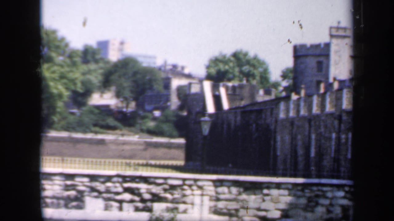 1949 England home-movie view of a historic stone fortification with crenellations, trees, and a park wall in the foreground.