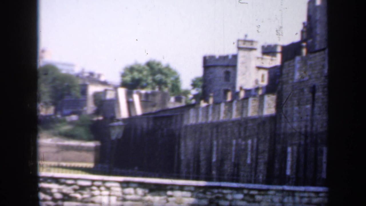 1949 8mm view of the Tower of London’s stone walls and turrets in bright daylight, with trees and a pale sky behind.