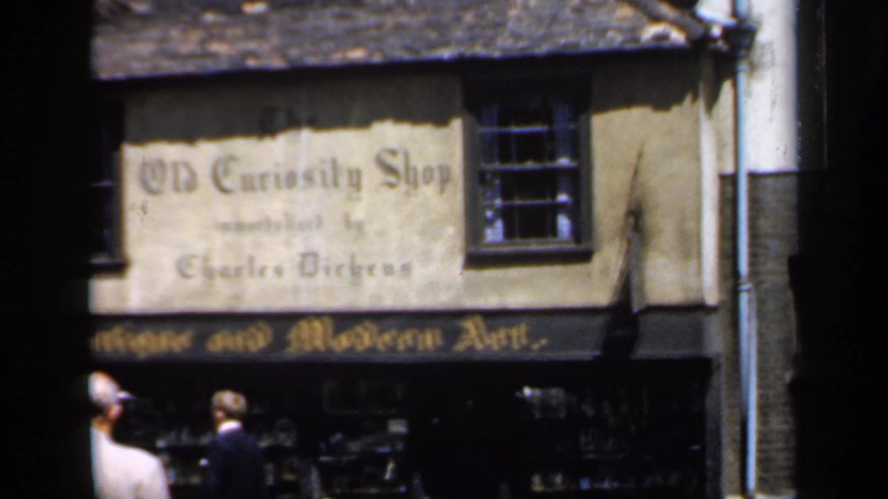 1949 England street view of The Old Curiosity Shop facade, antique art signboard, display windows, and adults walking past.