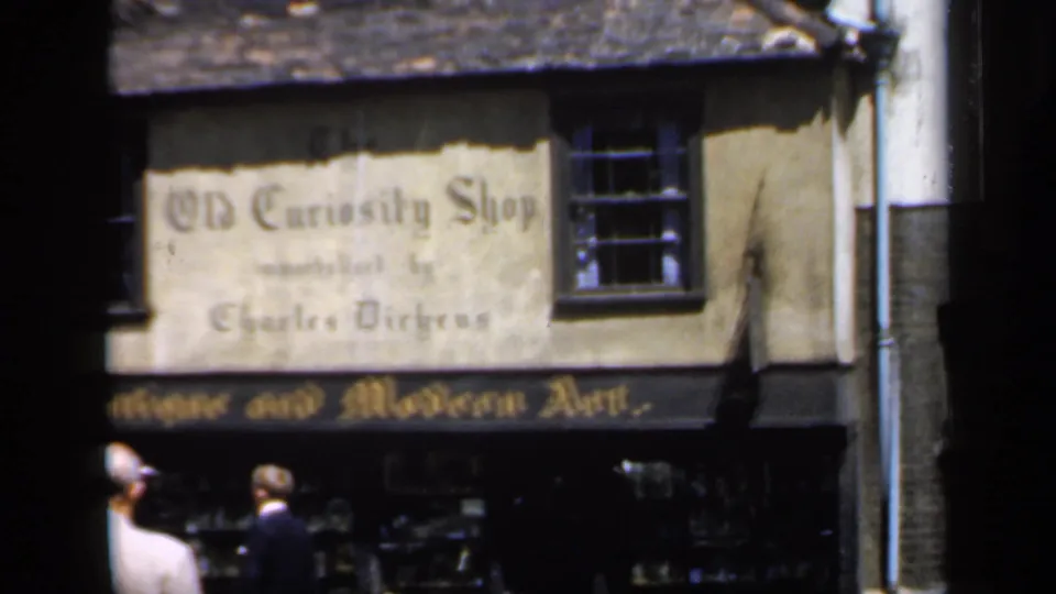 1949 England street view of The Old Curiosity Shop facade, antique art signboard, display windows, and adults walking past.
