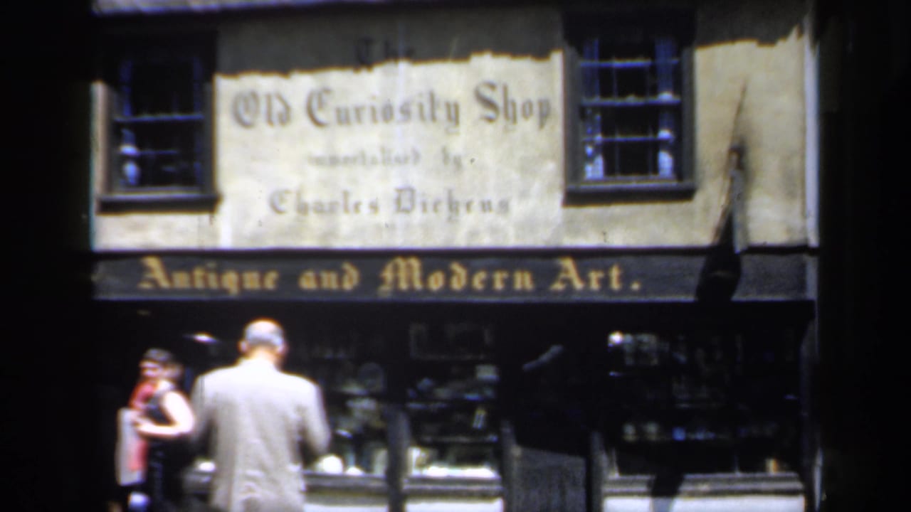 Pedestrians pass the Old Curiosity Shop storefront with antique and modern art lettering.