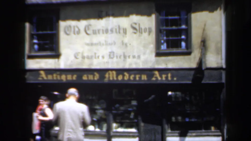 1949 England street view showing pedestrians outside the Old Curiosity Shop, with Charles Dickens wording and antique art signage visible.