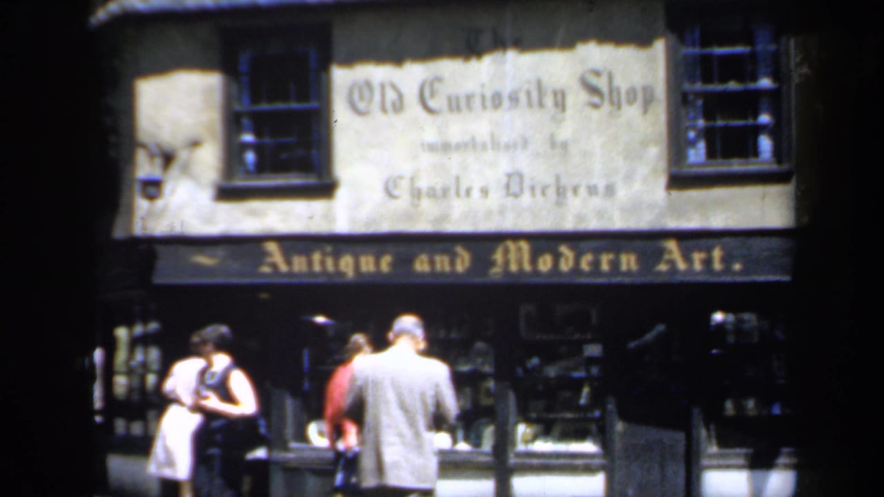 Street-level 1949 England view of people near the Old Curiosity Shop facade, with shop lettering and window displays in frame.