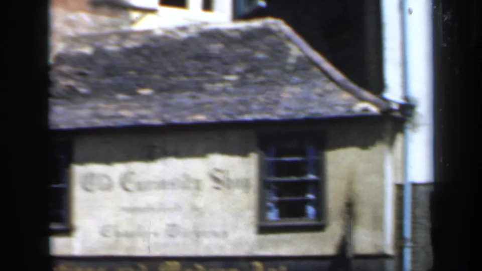 1949 England home-movie frame with a closer view of the Old Curiosity Shop wall sign and adjacent building edge.