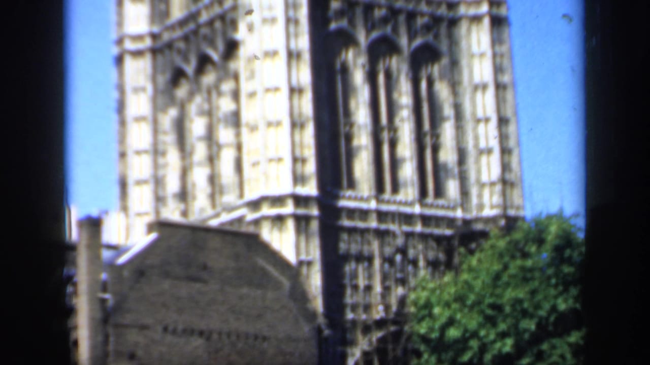 1949 England home-movie frame showing pale Gothic cathedral architecture, arched windows, blue sky, and trees.