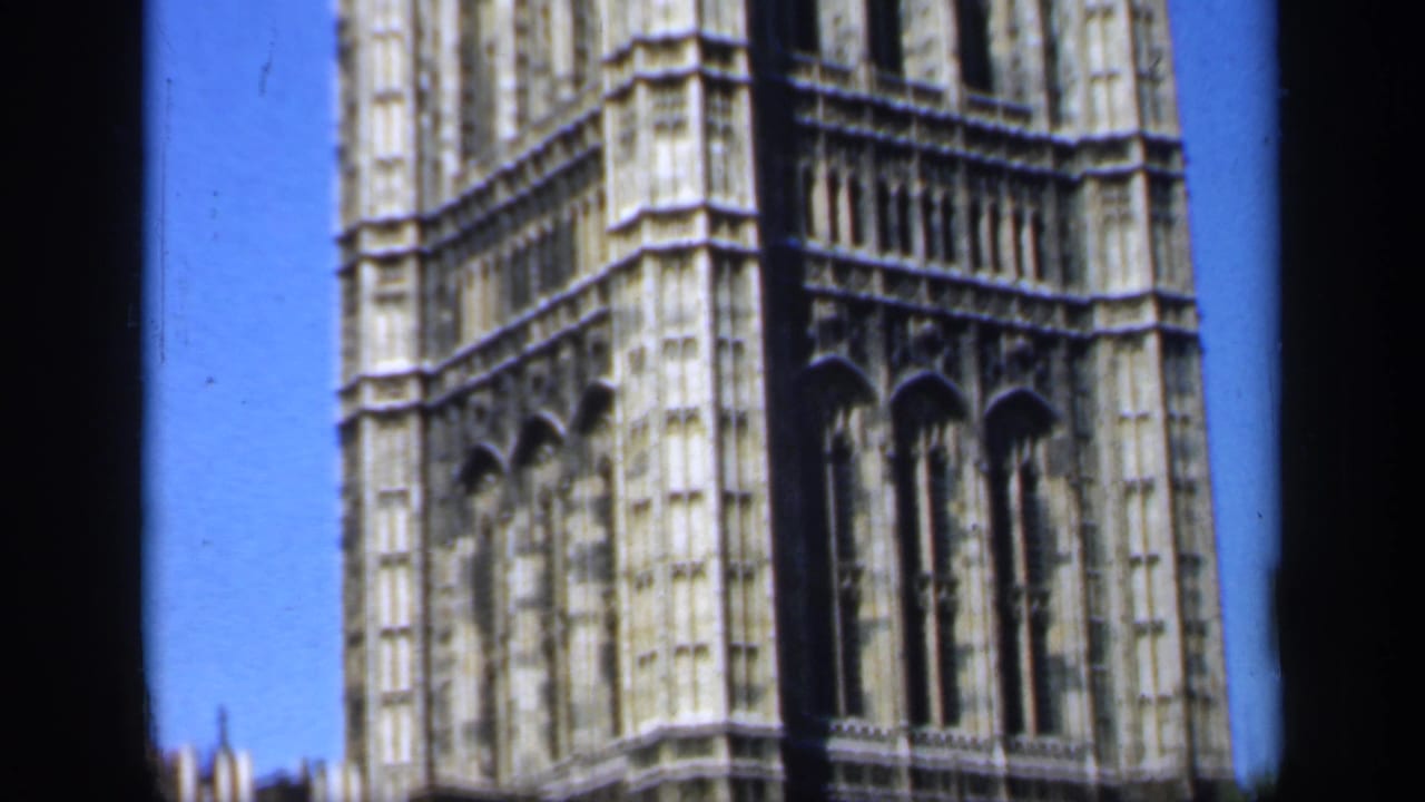 1949 England home-movie frame emphasizing Gothic cathedral buttresses, tall arched windows, and bright blue sky.