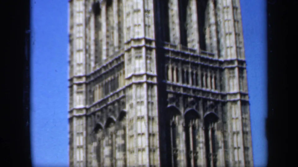 1949 England home-movie frame showing a close portion of an ornate Gothic landmark tower against a bright blue sky.
