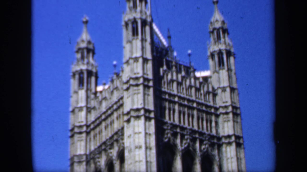 1949 England home-movie view of an ornate Gothic landmark roofline with small towers, spires, and pale stonework under blue sky.