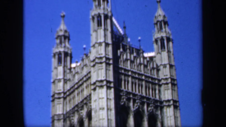 1949 England home-movie view of an ornate Gothic landmark roofline with small towers, spires, and pale stonework under blue sky.