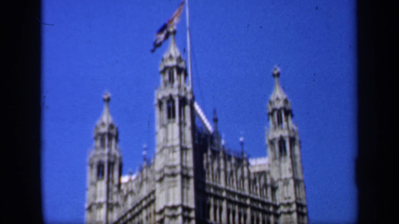 1949 England frame showing a Gothic landmark roofline with towers, spires, and a flag visible against the blue sky.