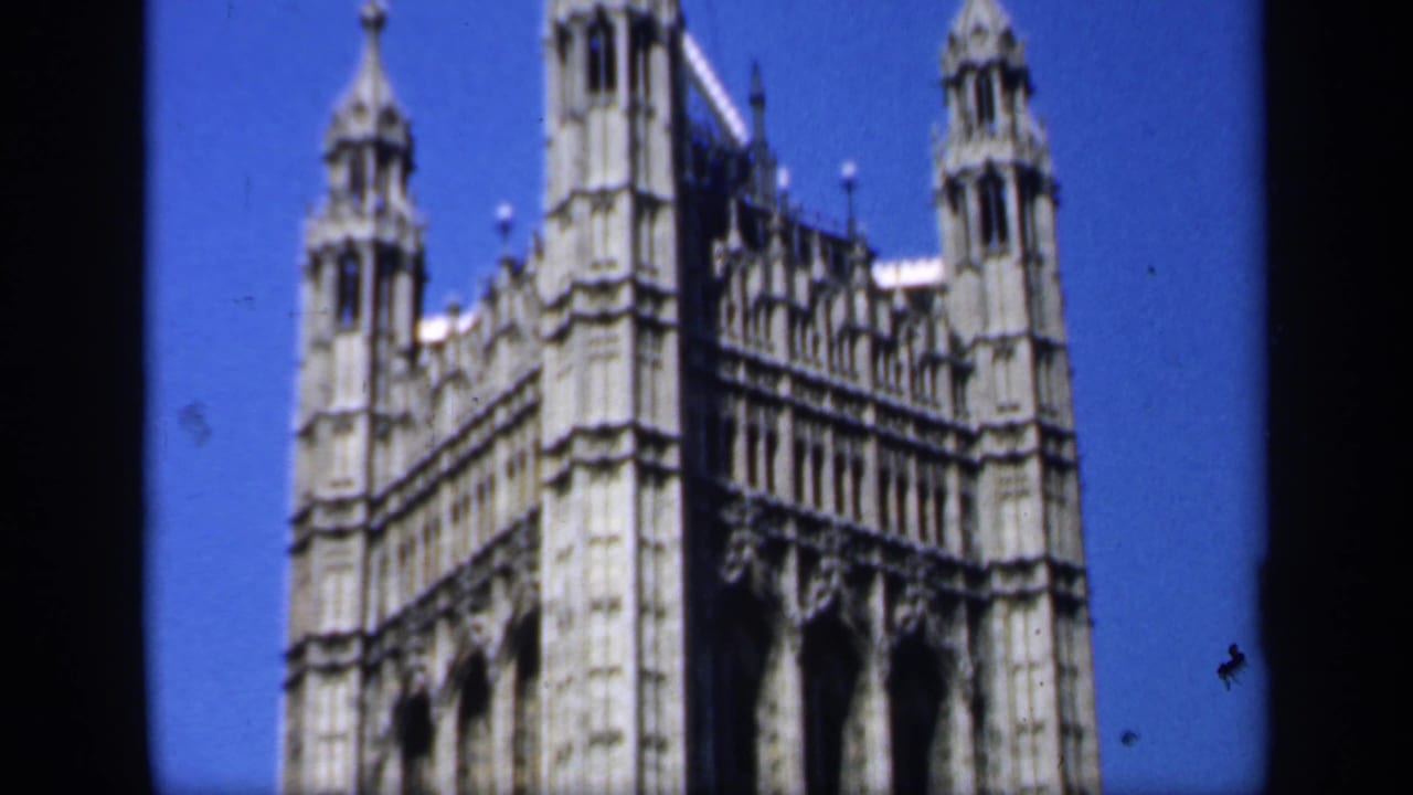 1949 England home-movie frame showing the Palace of Westminster facade and towers under a clear blue sky.