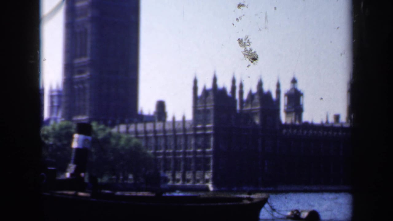 1949 8mm view of the Palace of Westminster across the Thames, framed from a boat with a standing person at left.