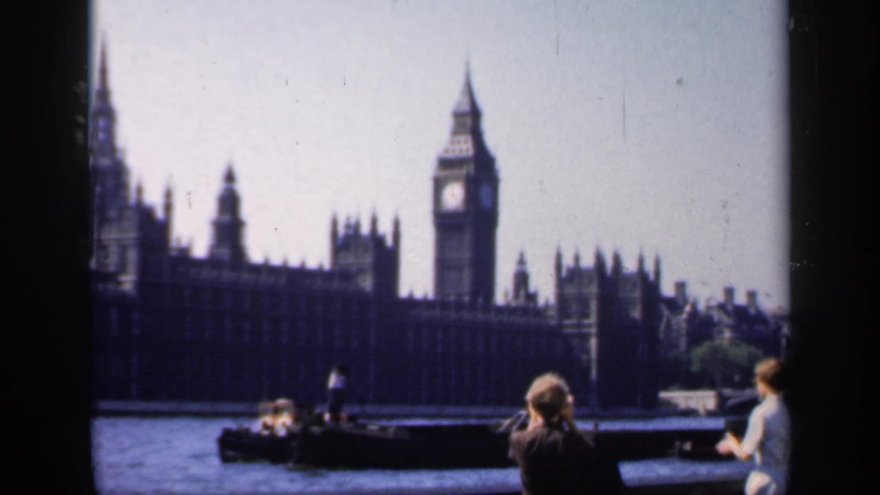 1949 London river view with Big Ben, the Houses of Parliament, a small boat, and tourists watching from the Thames embankment.