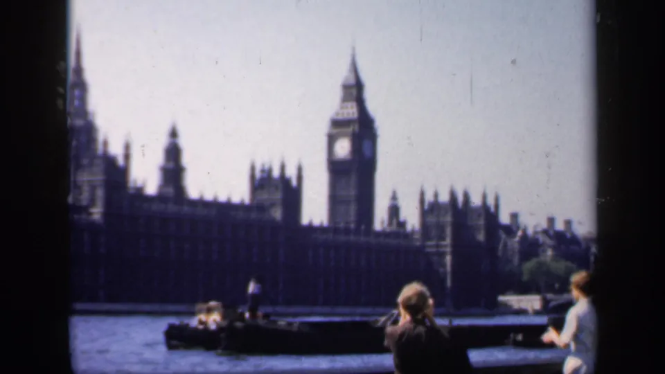 1949 London river view with Big Ben, the Houses of Parliament, a small boat, and tourists watching from the Thames embankment.