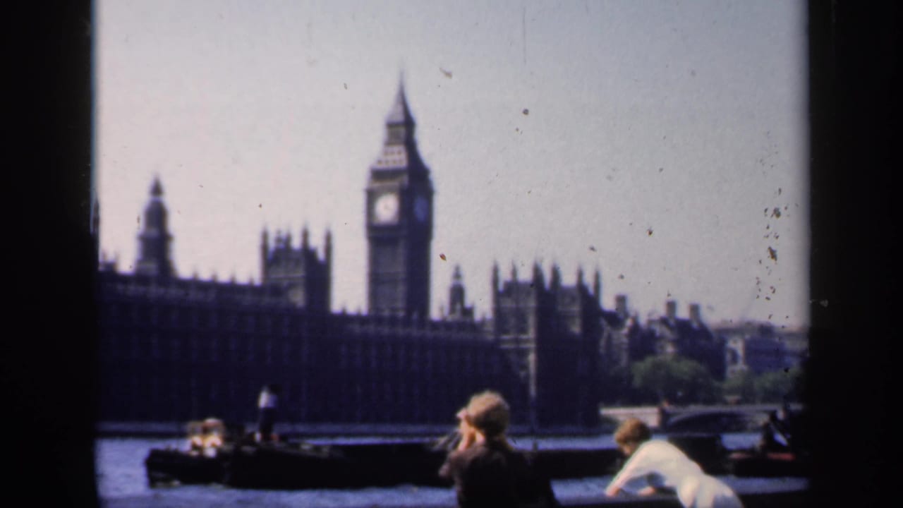 1949 8mm frame of Big Ben and Parliament across the Thames, with tourists in period clothing near the foreground railing.