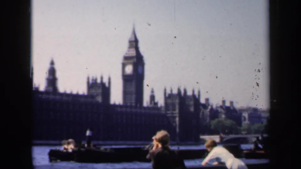 1949 8mm frame of Big Ben and Parliament across the Thames, with tourists in period clothing near the foreground railing.