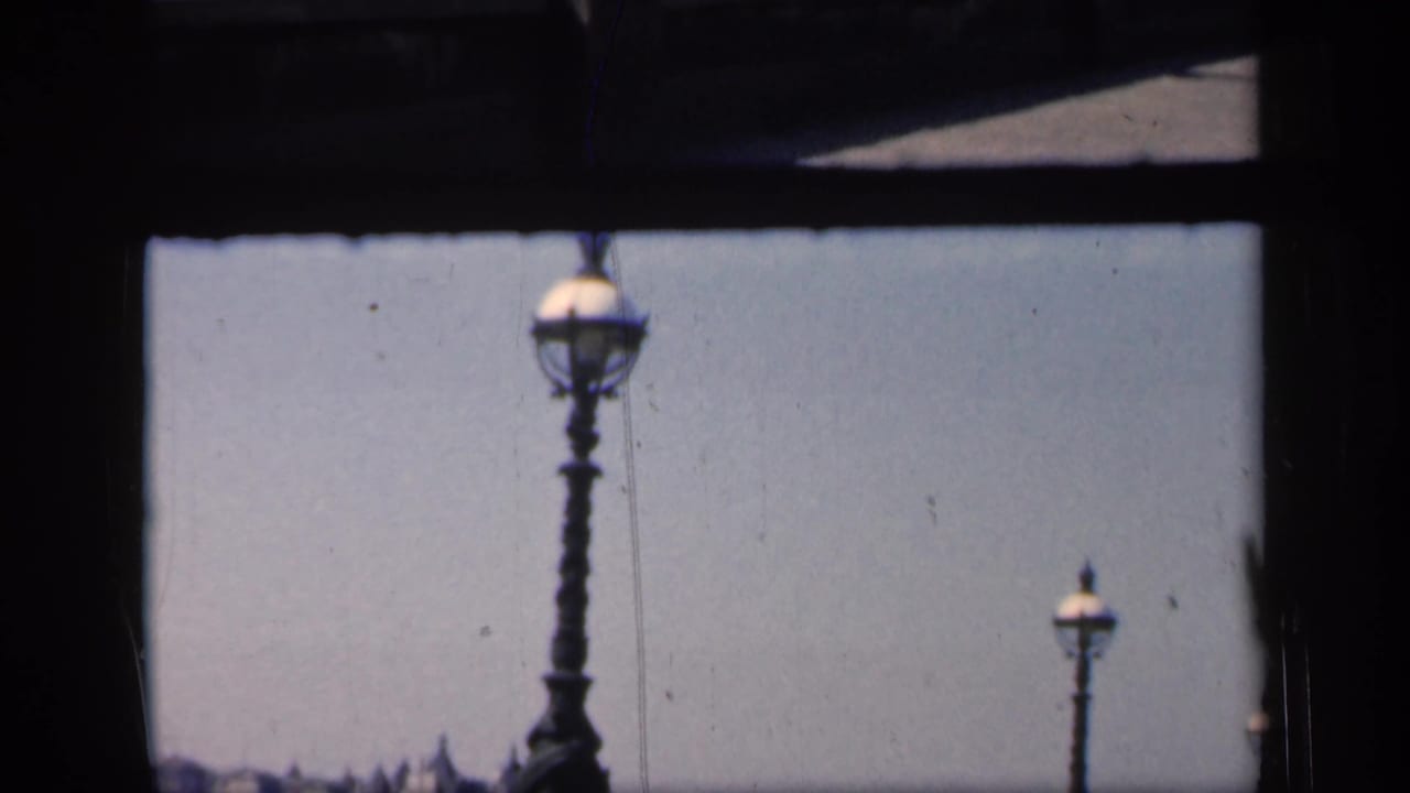 Dark bridge framing surrounds two ornate lampposts and a pale sky above a distant river view.