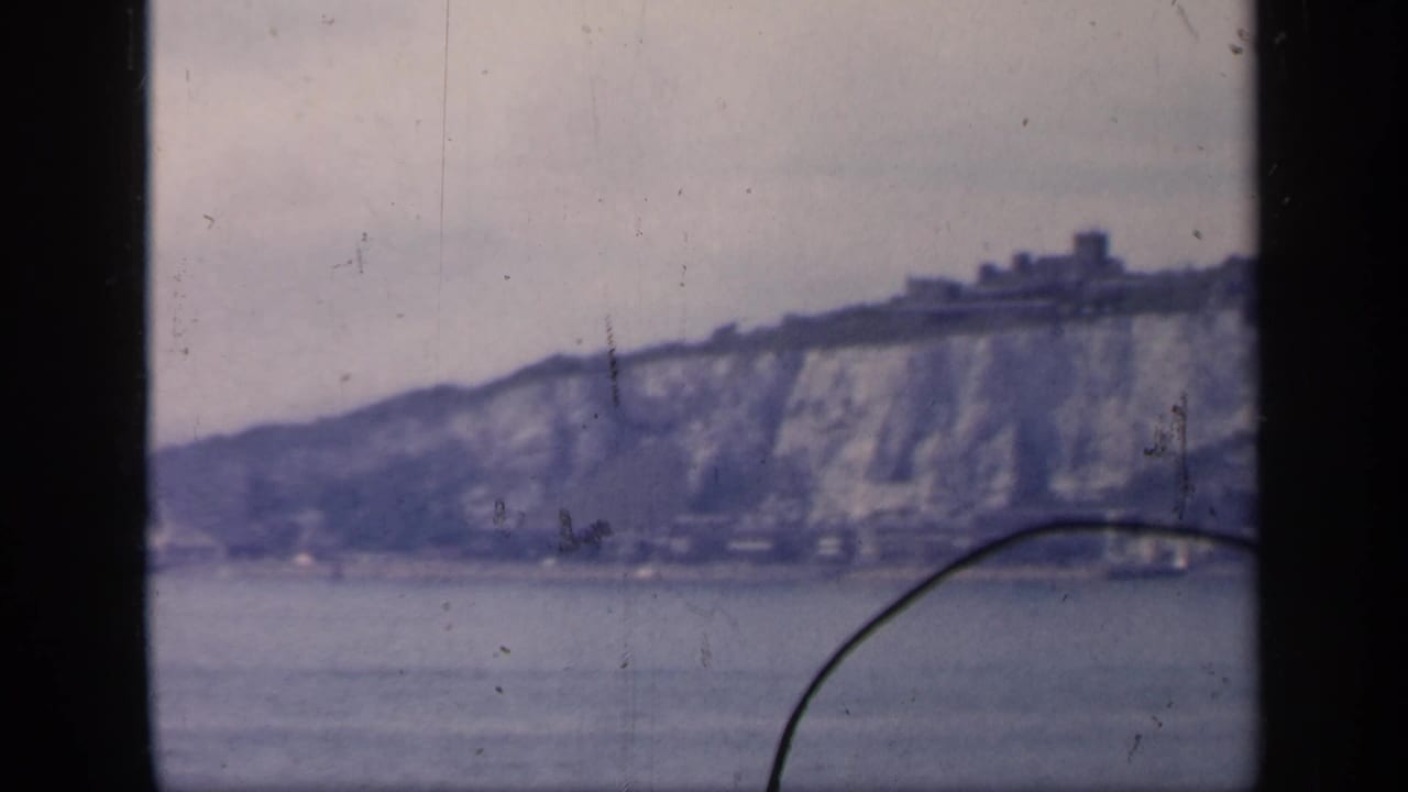 1949 England coastal view showing chalk cliffs, calm water, and a small distant structure on the ridge line.