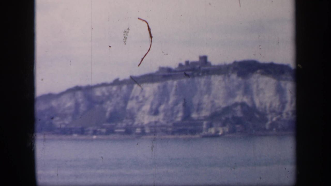 1949 England coastal frame with a distant ridge-top structure, pale chalk cliff, shoreline, and visible film wear.