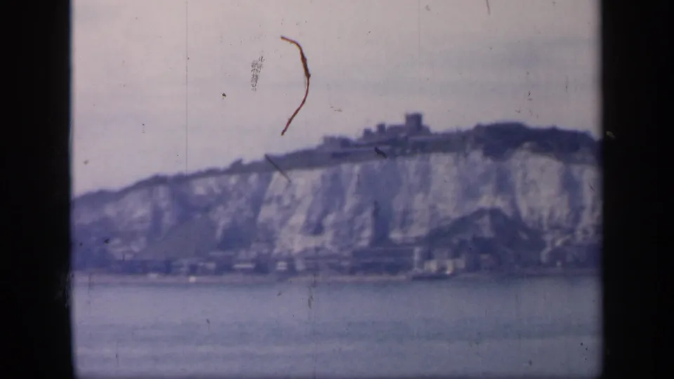 1949 England coastal frame with a distant ridge-top structure, pale chalk cliff, shoreline, and visible film wear.